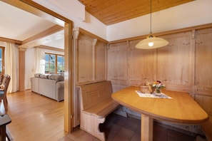 Un tavolo da pranzo in legno con una panca, un lampadario e vista su un soggiorno con divano e tende.