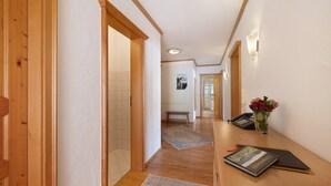 Un pasillo con suelo de madera, un banco, un florero con flores y un libro sobre una mesa.