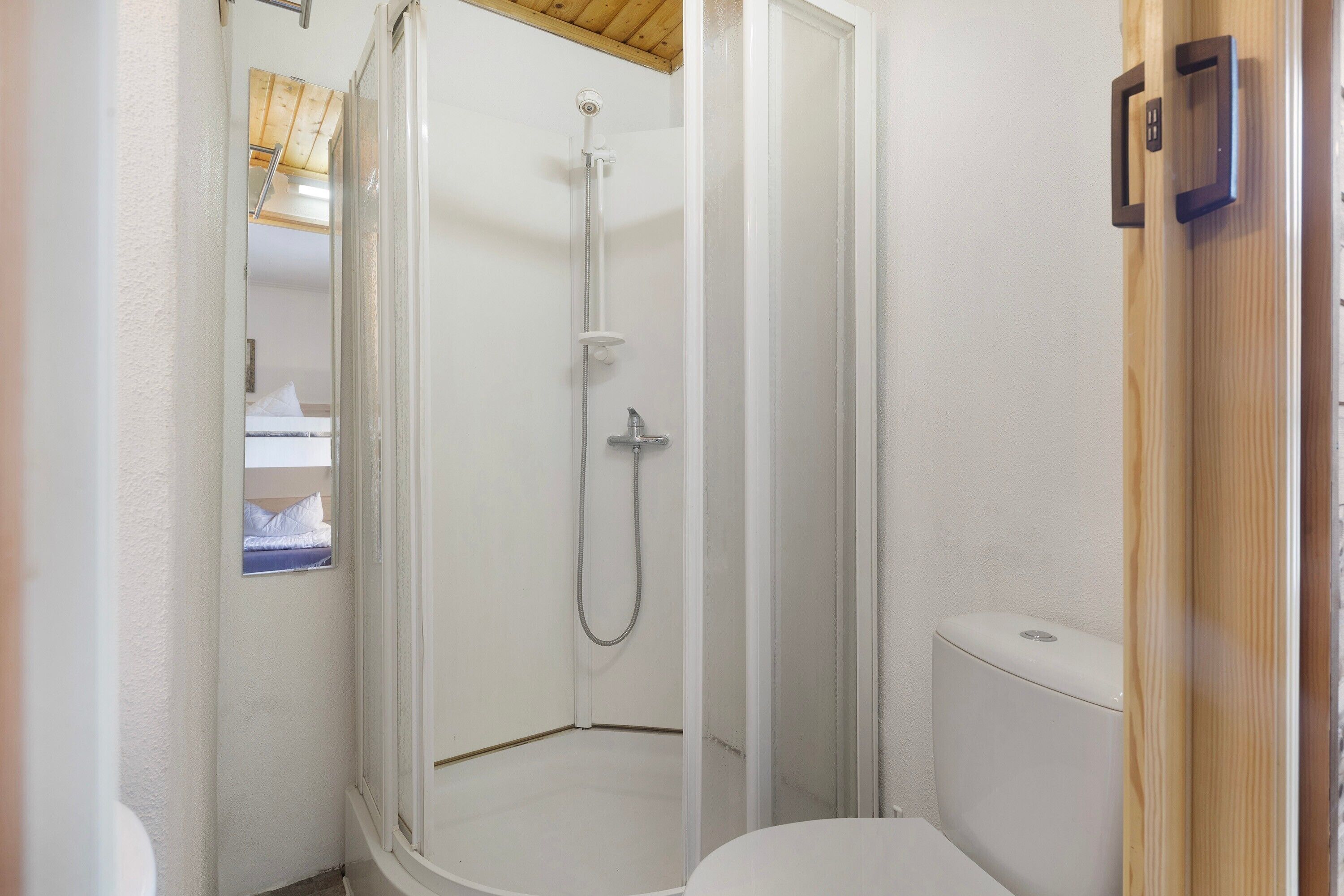 A shower with a glass door, a toilet, and a wooden ceiling.