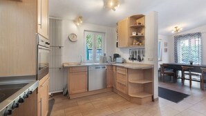 Une cuisine moderne avec des meubles en bois, un four encastré et un coin repas comprenant une table et des chaises.