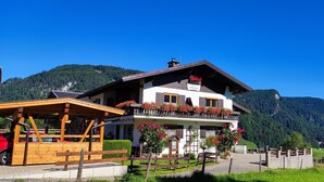 A two-story building with a balcony adorned with flowers, a wooden fence, and a mountain backdrop. - Holiday Apartment Rubihorn with Mountain View, Balcony and Wi-Fi (Oberstdorf)