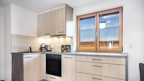 A modern kitchen with wooden cabinets, a dishwasher, and a large window with a view of solar panels. - Holiday Apartment Rubihorn with Mountain View, Balcony and Wi-Fi (Oberstdorf)