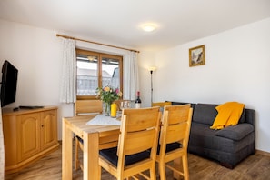 Ett rum med ett matbord, stolar, en soffa, en tv, ett fönster med gardiner och en lampa.
