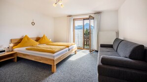 A bedroom with a bed, a sofa, a nightstand, a lamp, and a window with a view of mountains. - Apartment Nebelhorn with Mountain View, Balcony and Wi-Fi (Oberstdorf)