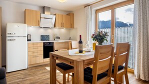 A modern kitchen with wooden cabinets, a dining table with chairs, and a view of mountains through the window. - Apartment Nebelhorn with Mountain View, Balcony and Wi-Fi (Oberstdorf)