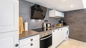 Eine moderne Küche mit Einbauofen, Mikrowelle, Kochfeld, Waschmaschine und Kaffeemaschine.