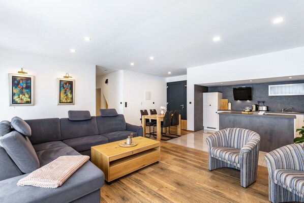 Ein modernes Wohnzimmer mit einem grauen Sofa, einem Holztisch, gestreiften Sesseln und einem Essbereich mit Tisch und Stühlen.
