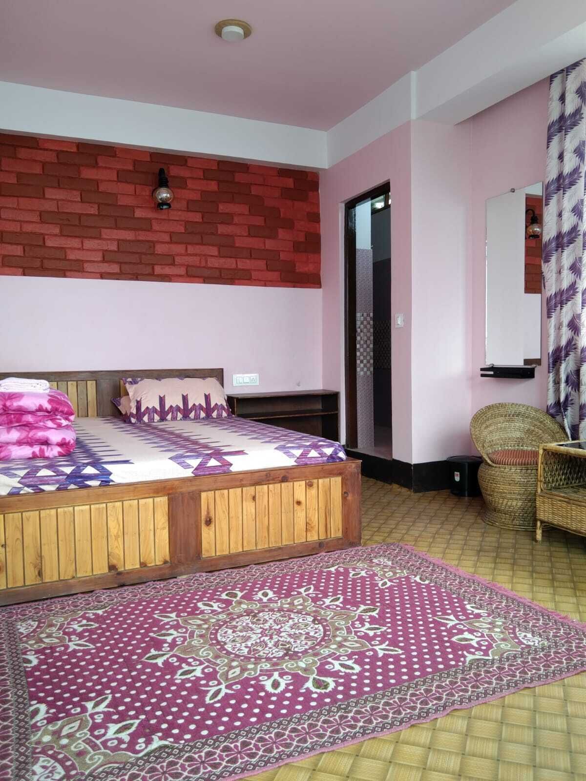 Un dormitorio con una cama de madera, un tapete estampado, una silla de mimbre y una pared de ladrillo decorativa.