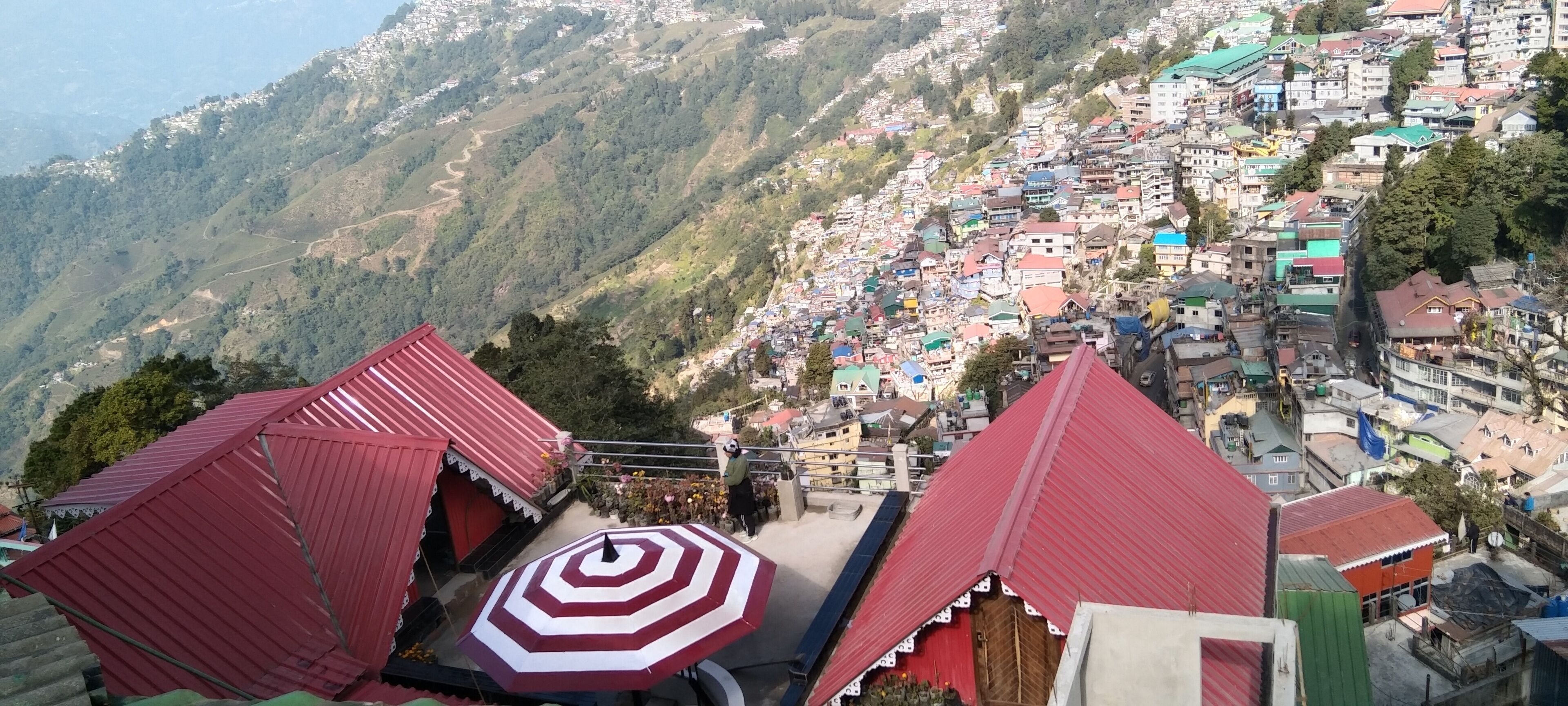 A mountainous town with terraced houses and a prominent red-roofed structure in the foreground.