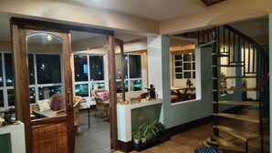 An interior with a staircase, a dining area, and a seating area with a view of the city at night. - Broadview Homestay  (Darjeeling)