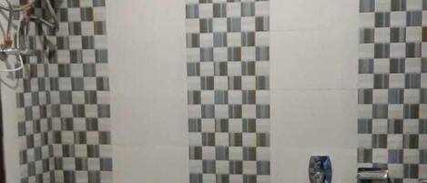 A bathroom with a toilet, a shower, and a tiled wall.