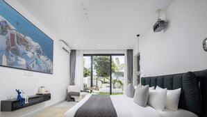 Une chambre moderne avec un grand lit, une vue sur l’extérieur, un tableau représentant un paysage côtier et une petite étagère ornée d’objets décoratifs.