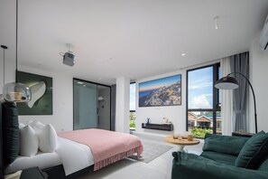 Una habitación de hotel moderna con una cama, un sillón verde, una mesita pequeña y un ventanal con vistas a la ciudad.