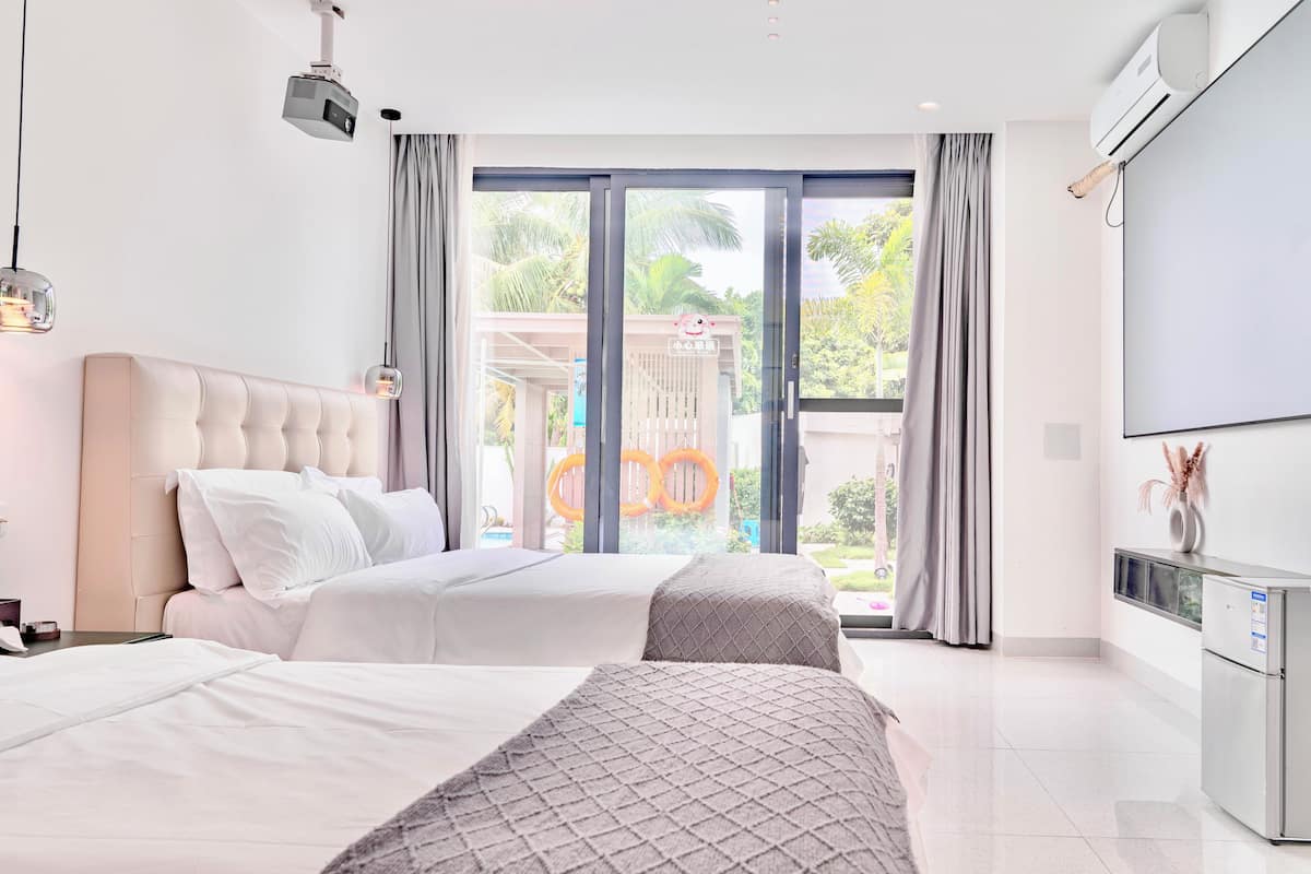 A modern hotel room with a large bed, a separate sofa, a flat-screen TV, and a balcony with a view of palm trees.