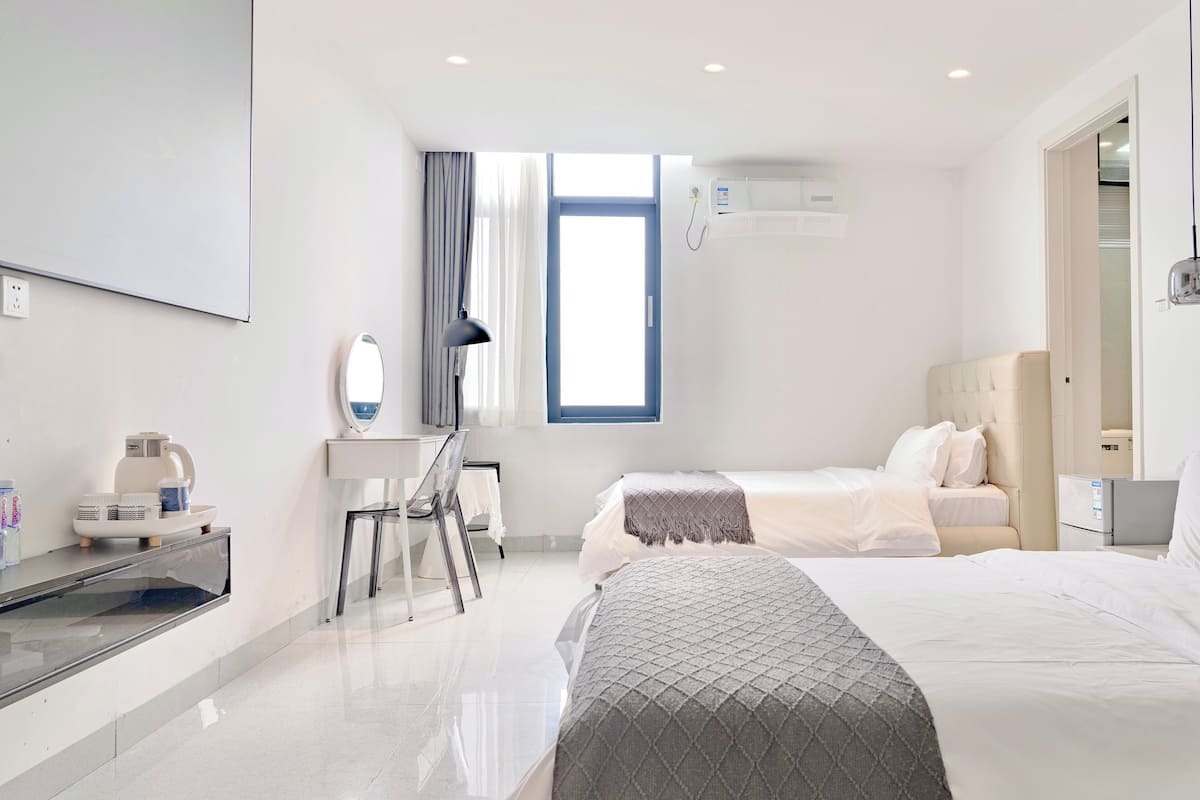A modern hotel room with a bed, bedside table, desk, chair, and a window with curtains.