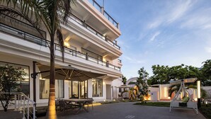 Un hôtel à plusieurs étages doté d’une terrasse, de palmiers et offrant une vue sur un ciel dégagé.