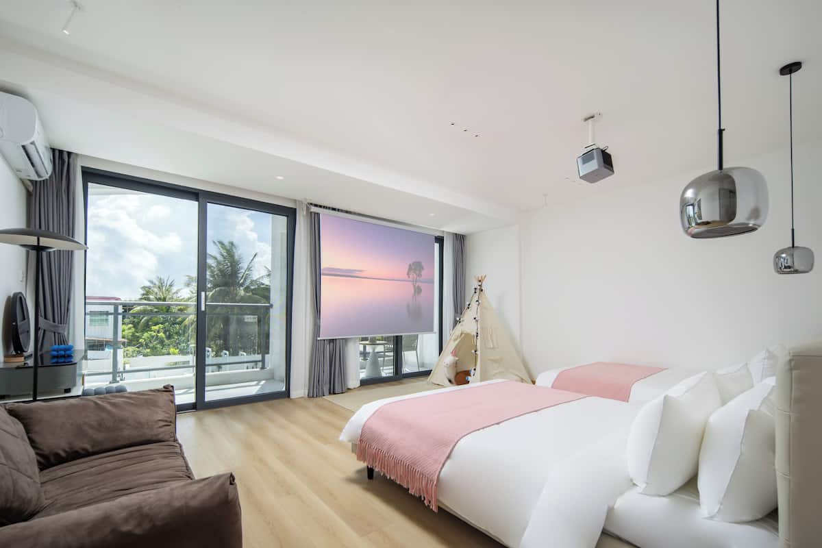 A modern hotel room with a large bed, a sofa, a TV, and a balcony with a view.