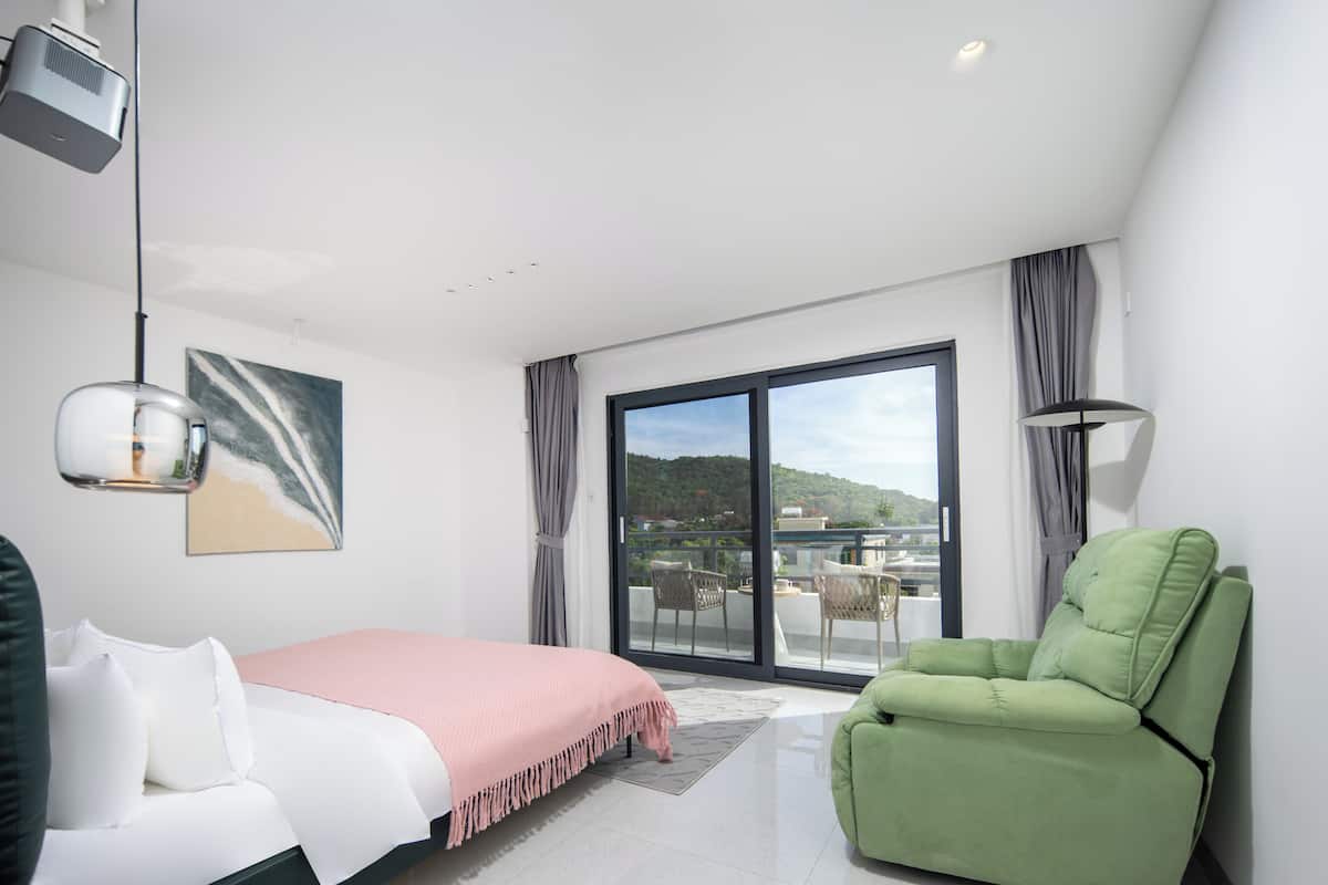A modern bedroom with a bed, a green chair, a balcony with a view, and a projector.