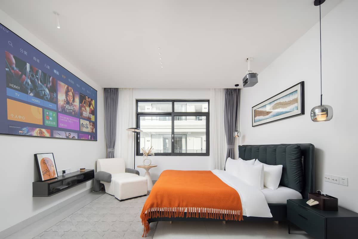 A modern hotel room with a large bed, a desk, a chair, a TV mounted on the wall, and a window with curtains.