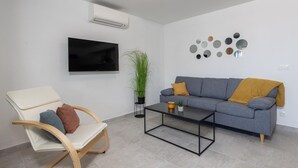 A modern living room with a grey sofa, a wooden rocking chair, a coffee table, and a mounted TV. - Family-Friendly Apartment Near the Coast (Crikvenica)