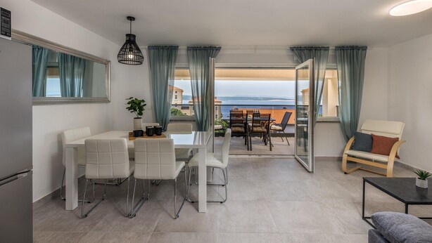 A modern living room with a dining area, a sofa, and a view of the sea.