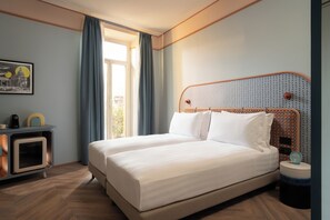 Une chambre d’hôtel avec un grand lit, un petit bureau avec une lampe et une fenêtre avec des rideaux.