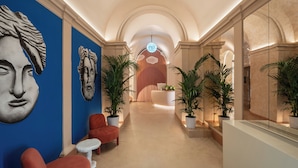 A hallway with a blue wall, red chairs, a white table, and potted plants. - Cloud 7 Roma Hotel (Rome)