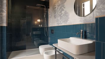 Uma casa de banho moderna com banheira, sanita e bidé, apresentando azulejos azul escuro e um espelho grande.