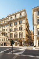 Un edificio storico dall'architettura classica, un attraversamento pedonale e passanti.