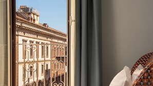 A hotel room with a bed, a window with curtains, and a view of a building with classical architecture. - Cloud 7 Roma Hotel (Rome)