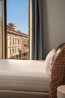 Una camera d'hotel con un letto, una finestra con tende e vista su un edificio dall'architettura classica.