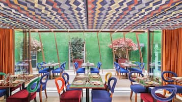A restaurant with colorful chairs and tables, large windows, and a patterned ceiling.