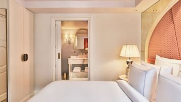 A hotel room with a large bed, a nightstand with a lamp, a bathroom visible through an open door, and a decorative wall panel.