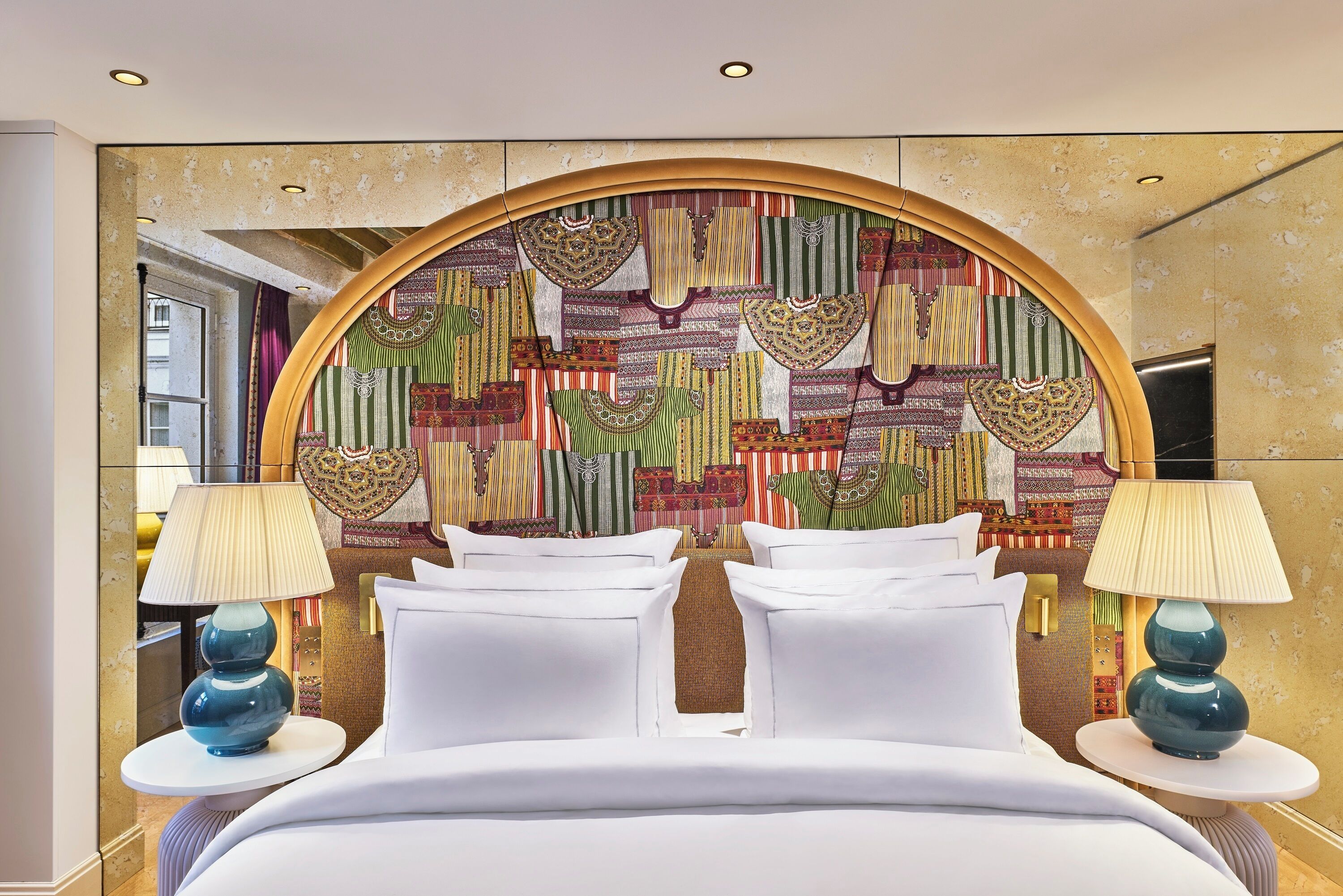 A hotel room with a large bed, two bedside tables with lamps, and a colorful wall tapestry.