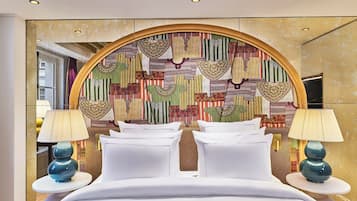 A hotel room with a large bed, two bedside tables with lamps, and a colorful wall tapestry.