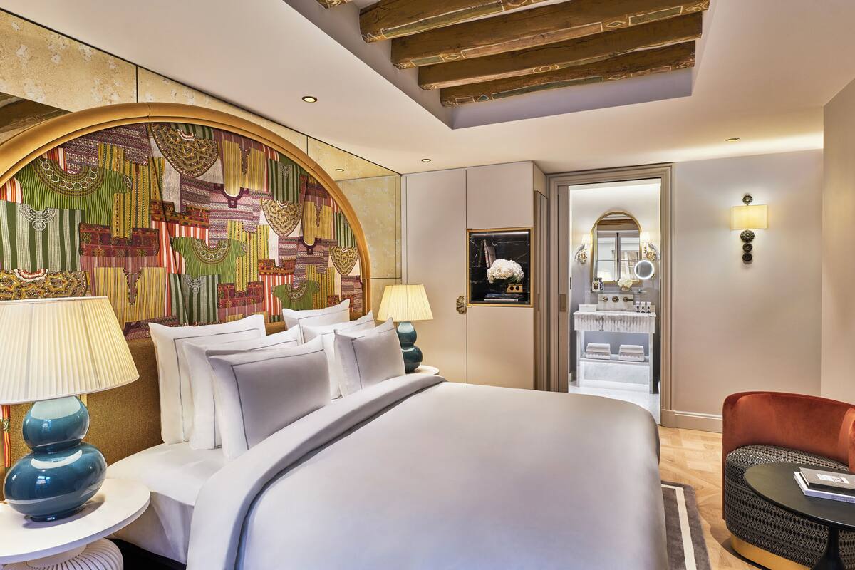 A hotel room with a large bed, two bedside tables with lamps, a red chair, and a mirror with a light.