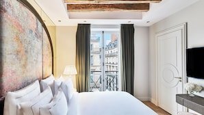 Habitación de hotel con una cama grande, vistas a edificios a través de una ventana y un televisor sobre un soporte.