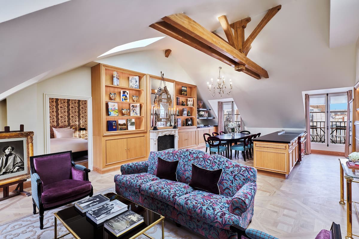 A spacious loft with a high ceiling, wooden beams, a large sofa, a dining area, and a kitchen.