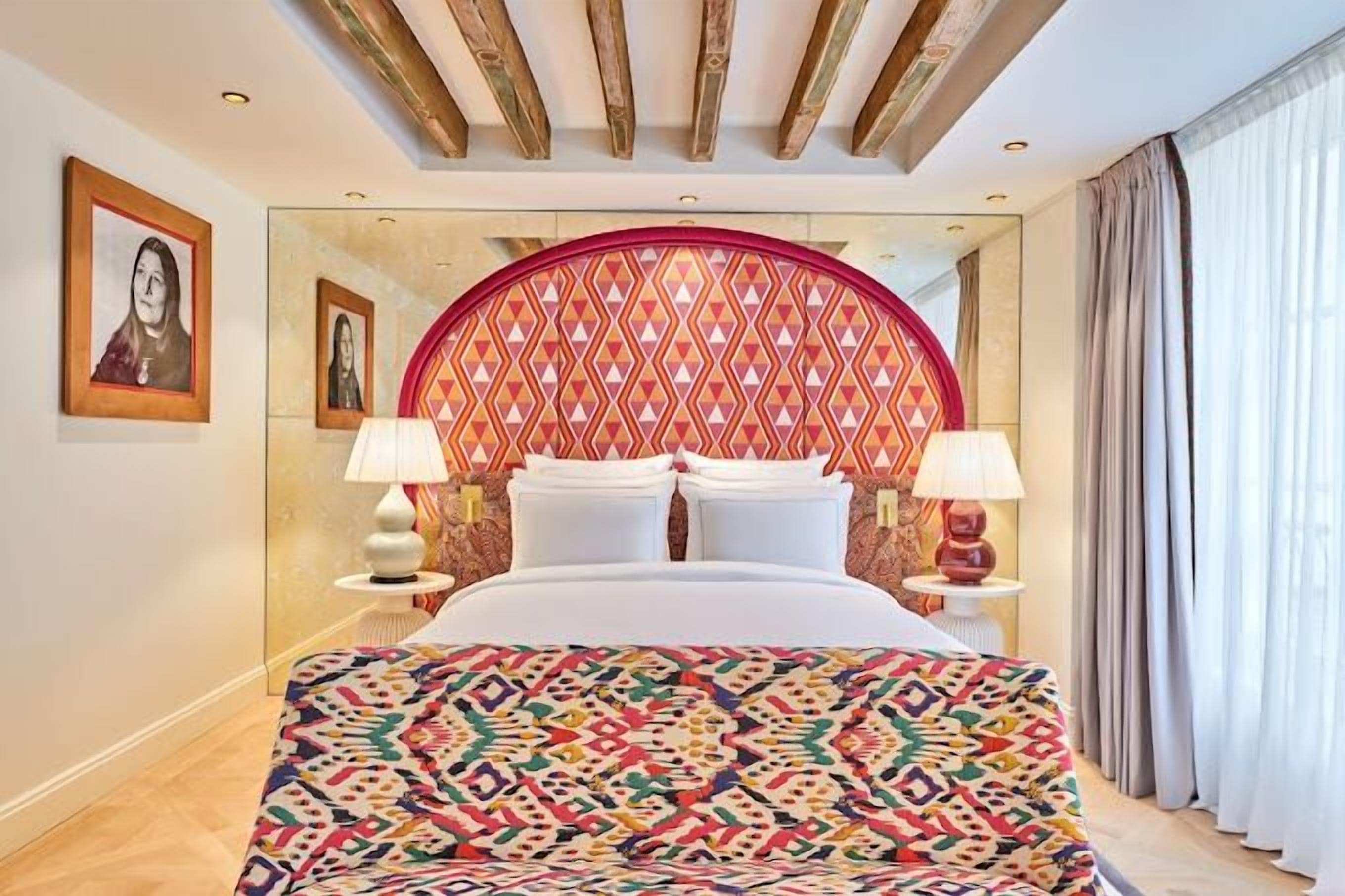 A hotel room with a large bed, two bedside lamps, a patterned headboard, and framed artwork on the walls.