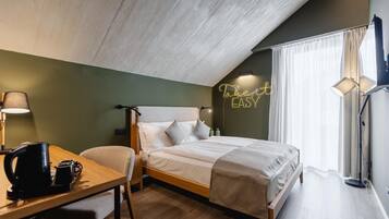 Quarto de hotel bem arrumado com uma cama, uma escrivaninha com um chaleira, uma cadeira, uma luminária de cabeceira e um letreiro de neon na parede.