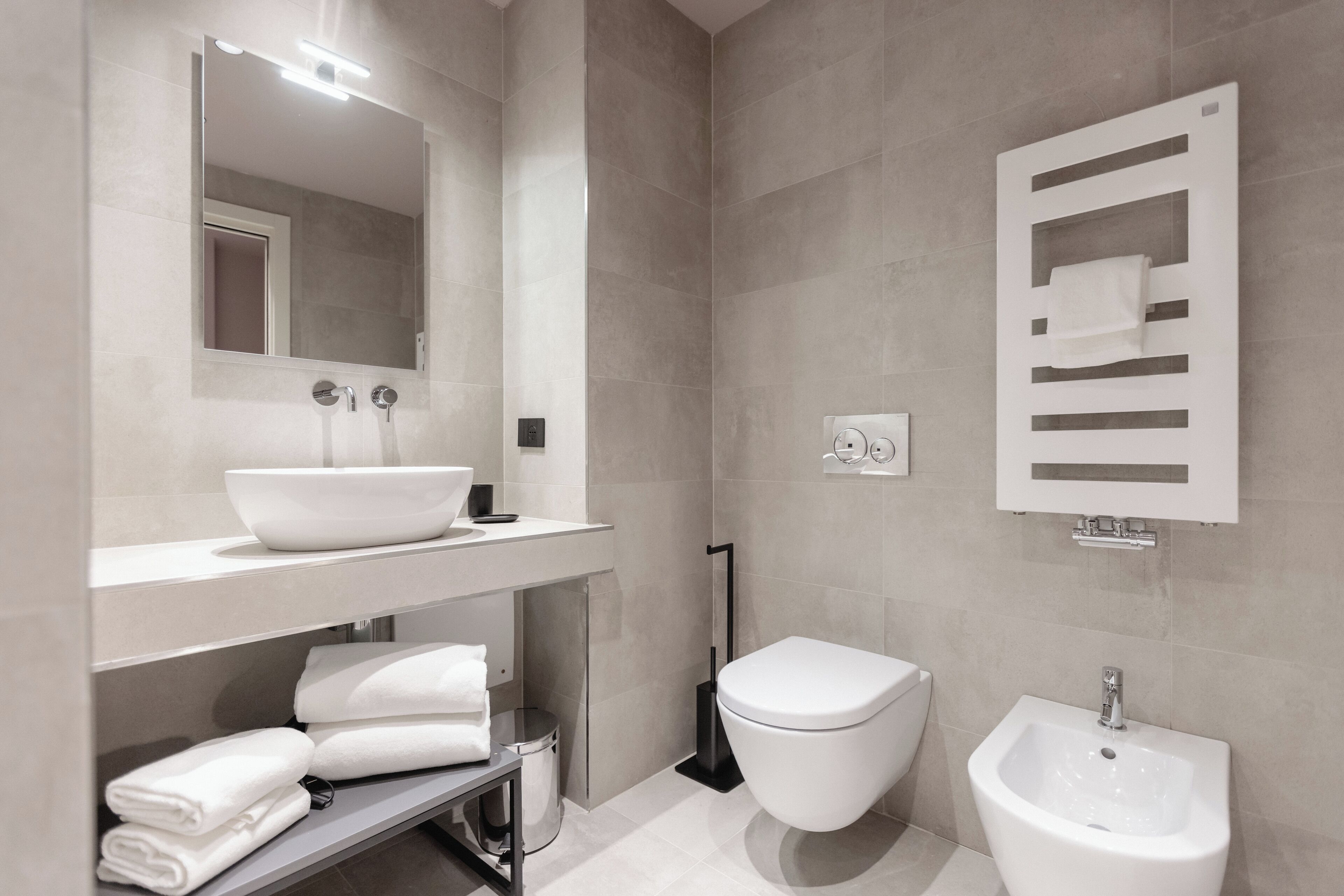 Un baño moderno con un espejo grande, un lavabo, un inodoro y un bidé.