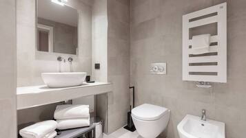 Un baño moderno con un espejo grande, un lavabo, un inodoro y un bidé.