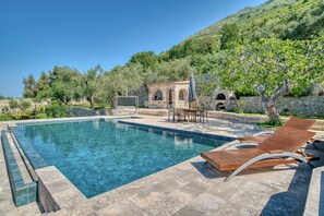 A swimming pool with lounge chairs, a stone building with arches, and a hillside with trees. - Spacious Villa Olive Grove with private Pool (Budva)