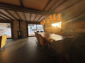 Ein stilvoller Essbereich mit einem langen Tisch, Stühlen, einer Steinwand und Blick durch große Fenster.