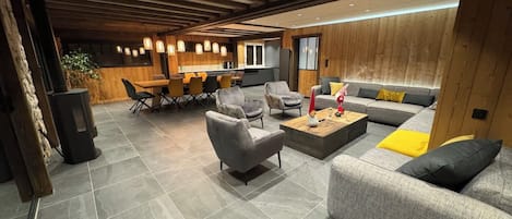 A modern living room with a sofa, armchairs, and a coffee table. There is a dining area with chairs and a table in the background.