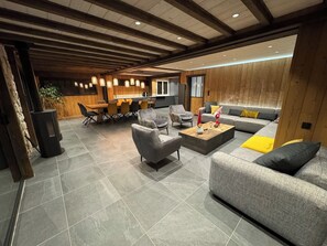 A modern living room with a sofa, armchairs, and a coffee table. There is a dining area with chairs and a table in the background.