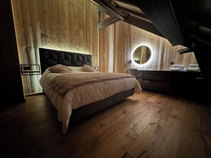 A bedroom with a large bed, wooden walls, a circular mirror, and a built-in bench.