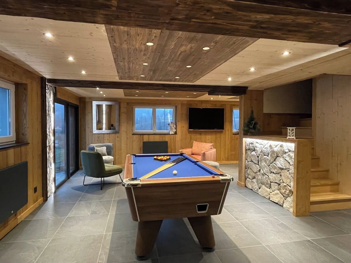 A pool table in a room with a stone wall, a sofa, and a television.