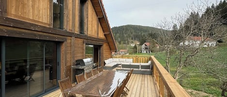 A wooden deck with a dining table and chairs, a barbecue grill, and a sofa.