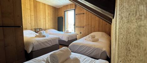 Una habitación con tres camas, paredes de madera y techo inclinado.